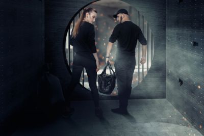 woman and man dressed in black with bag in hands leaving through the open bank cell door
